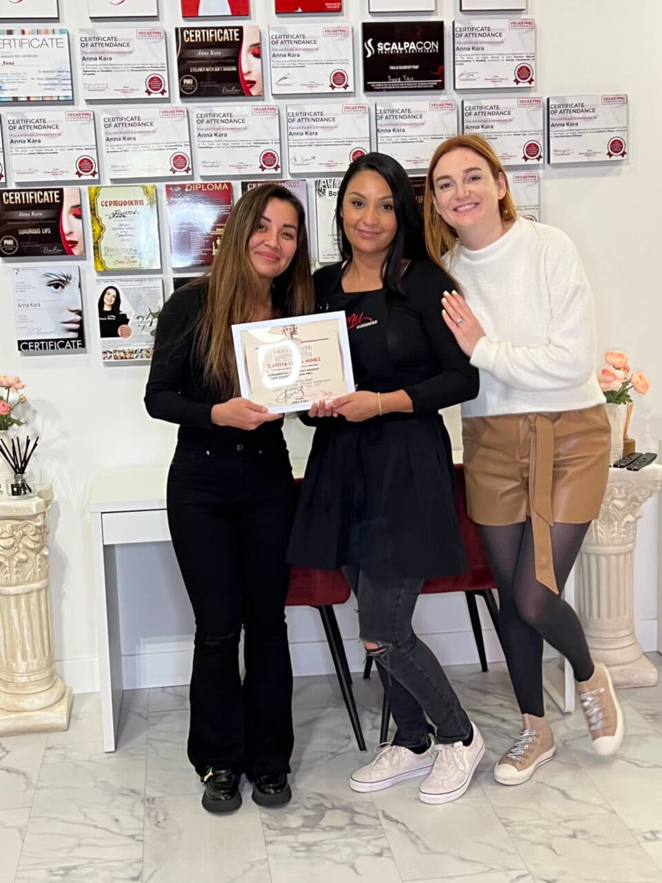 Graduates with their certificates in front of the certificate wall