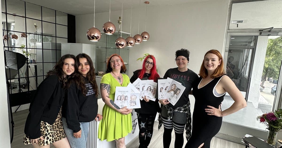 A group of six women holding course certificates in the downtown studio under copper pendant lamps
