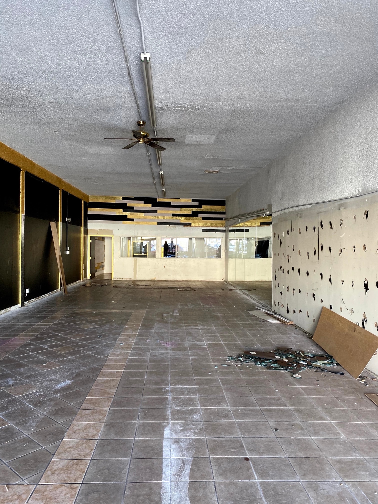 Empty hall with an old tile floor, bare walls and a ceiling fan, before the renovation