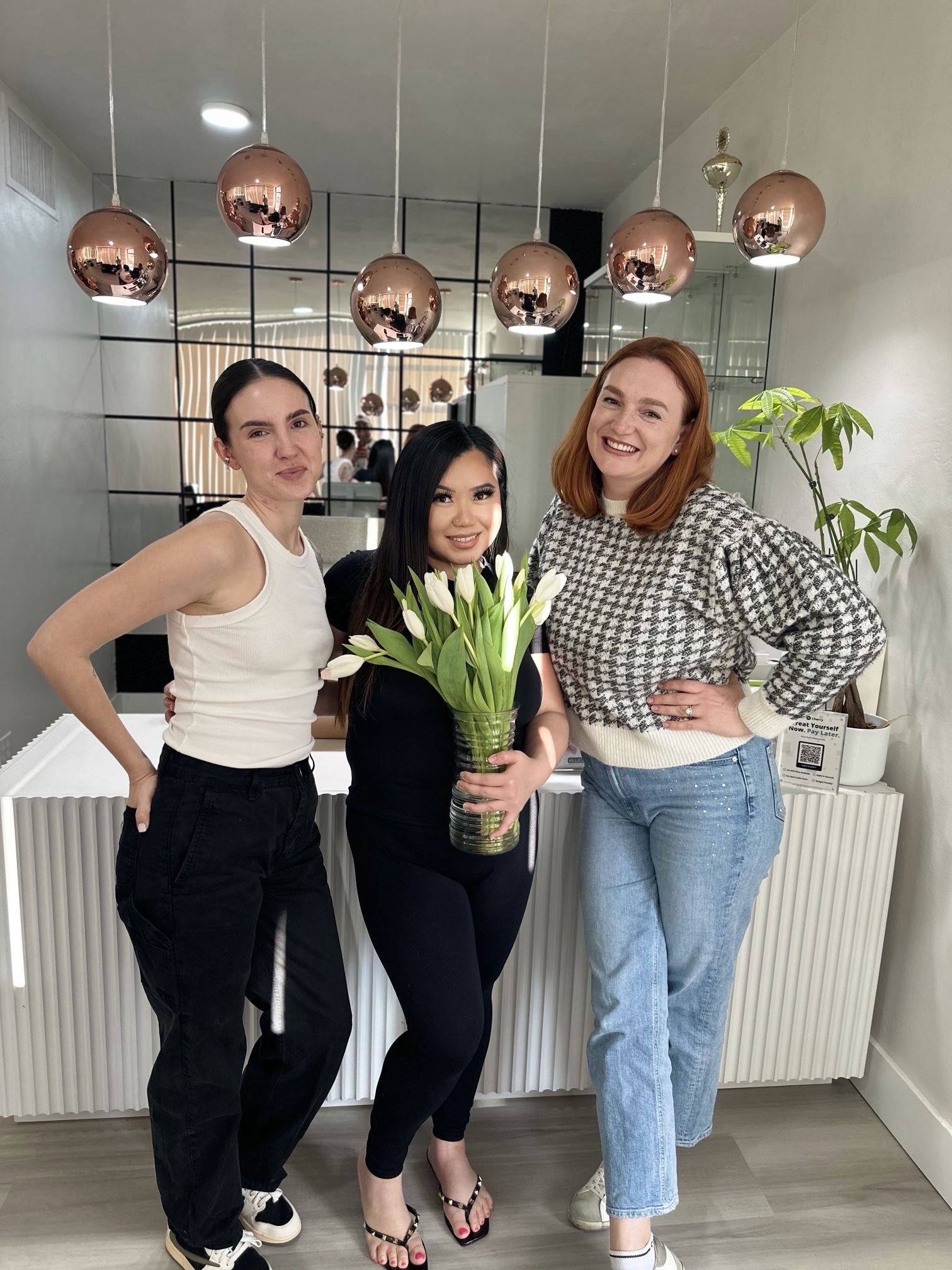 Anna Kara with two students standing in front of the white ribbed reception desk under copper pendant lamps