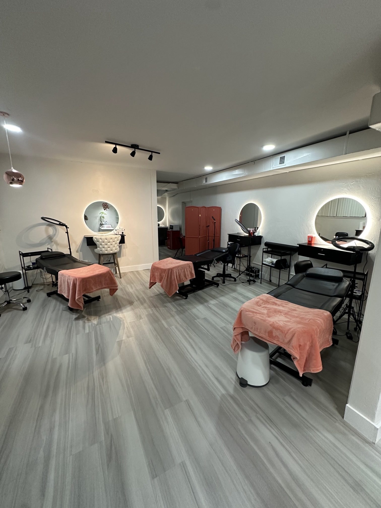 The renovated downtown hall with three treatment beds, round backlit mirrors and a gray wood-look floor