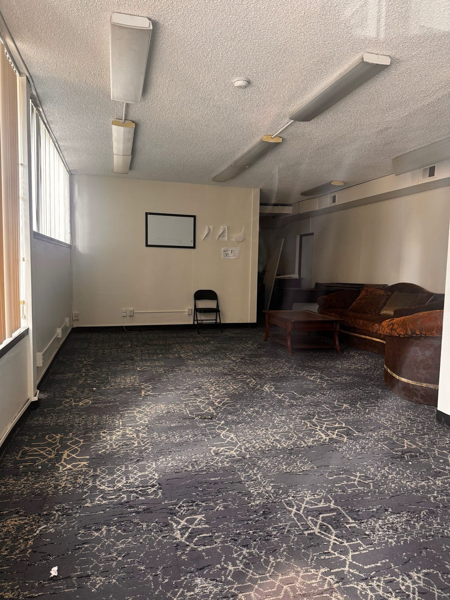 The downtown space before the renovation: dark patterned carpet, fluorescent ceiling lights and an old sofa
