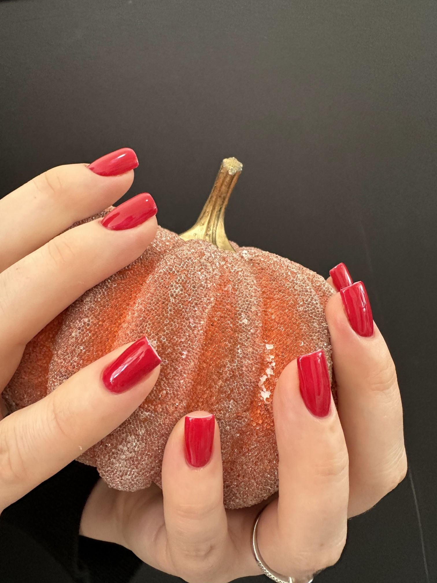 Hands with red gel nails holding a glittery orange decorative pumpkin
