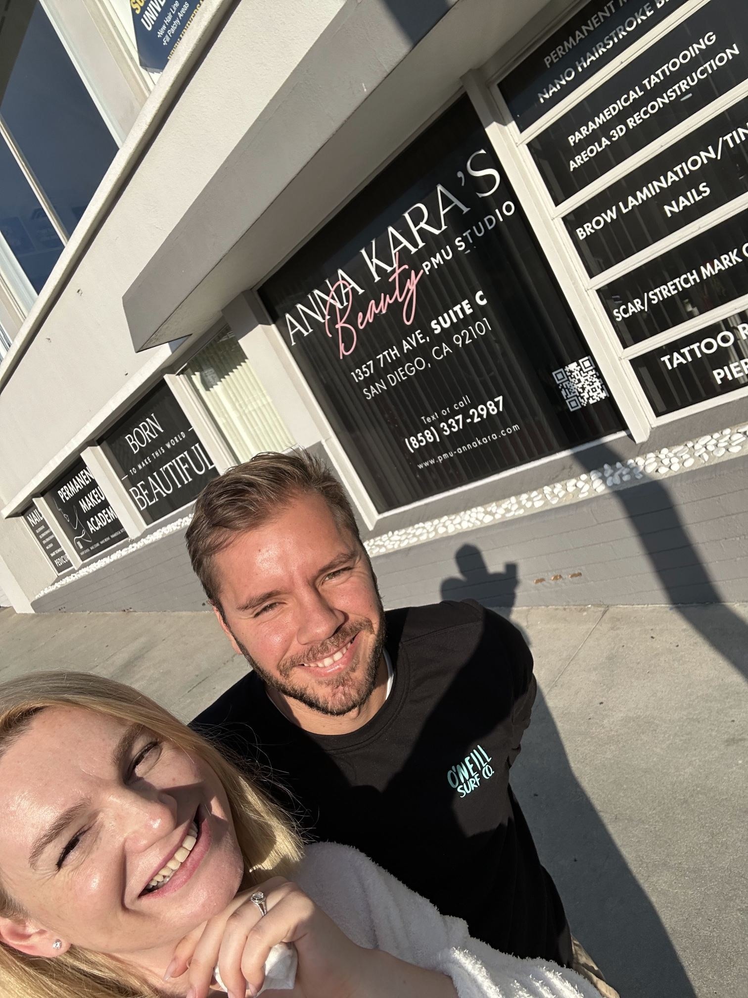 Alex and Anna Kara smiling in front of the finished storefront windows showing the studio logo, services, address and phone number