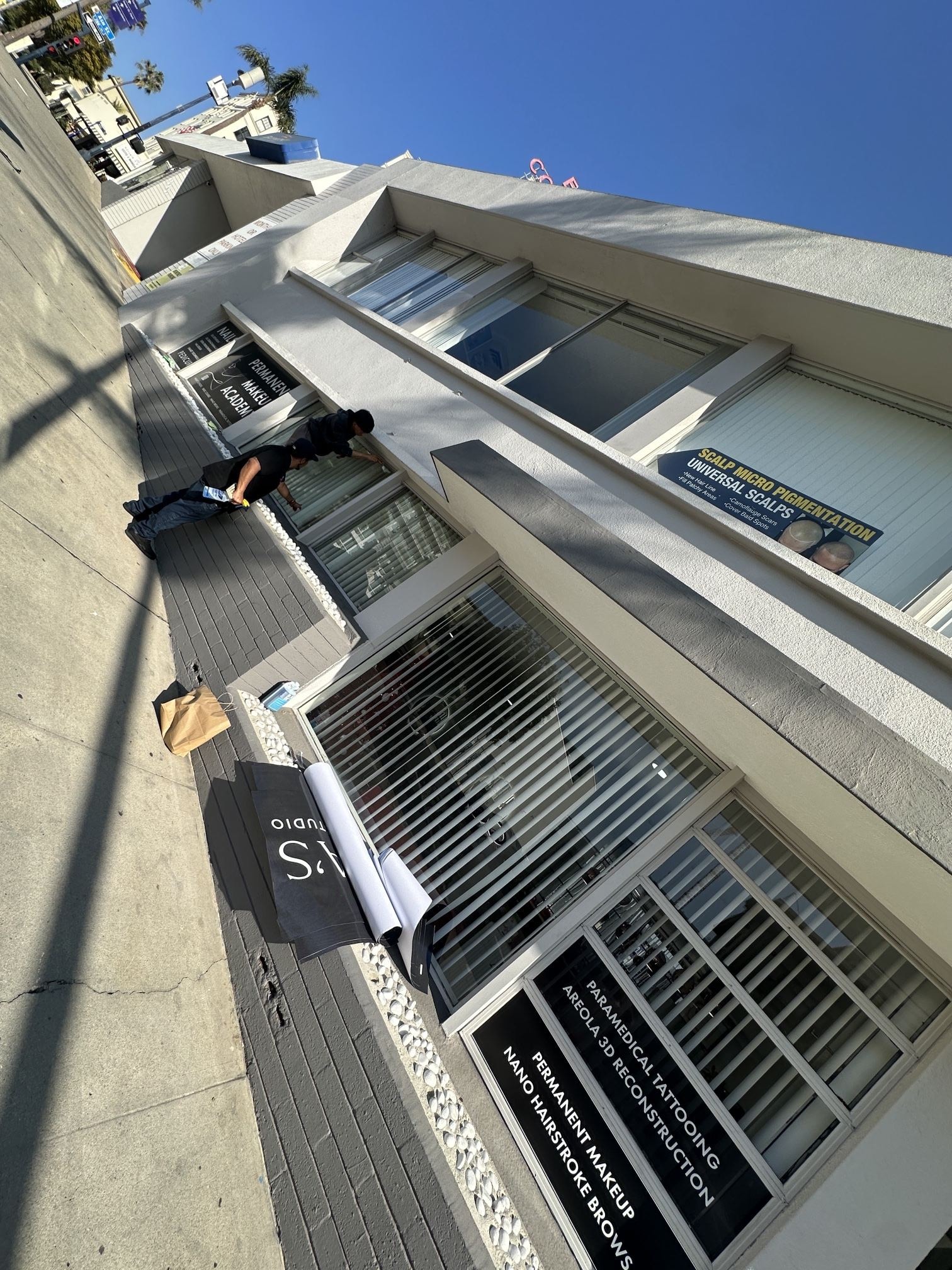 Installers working on the storefront windows of the downtown studio, with the first window graphics laid out on the sidewalk
