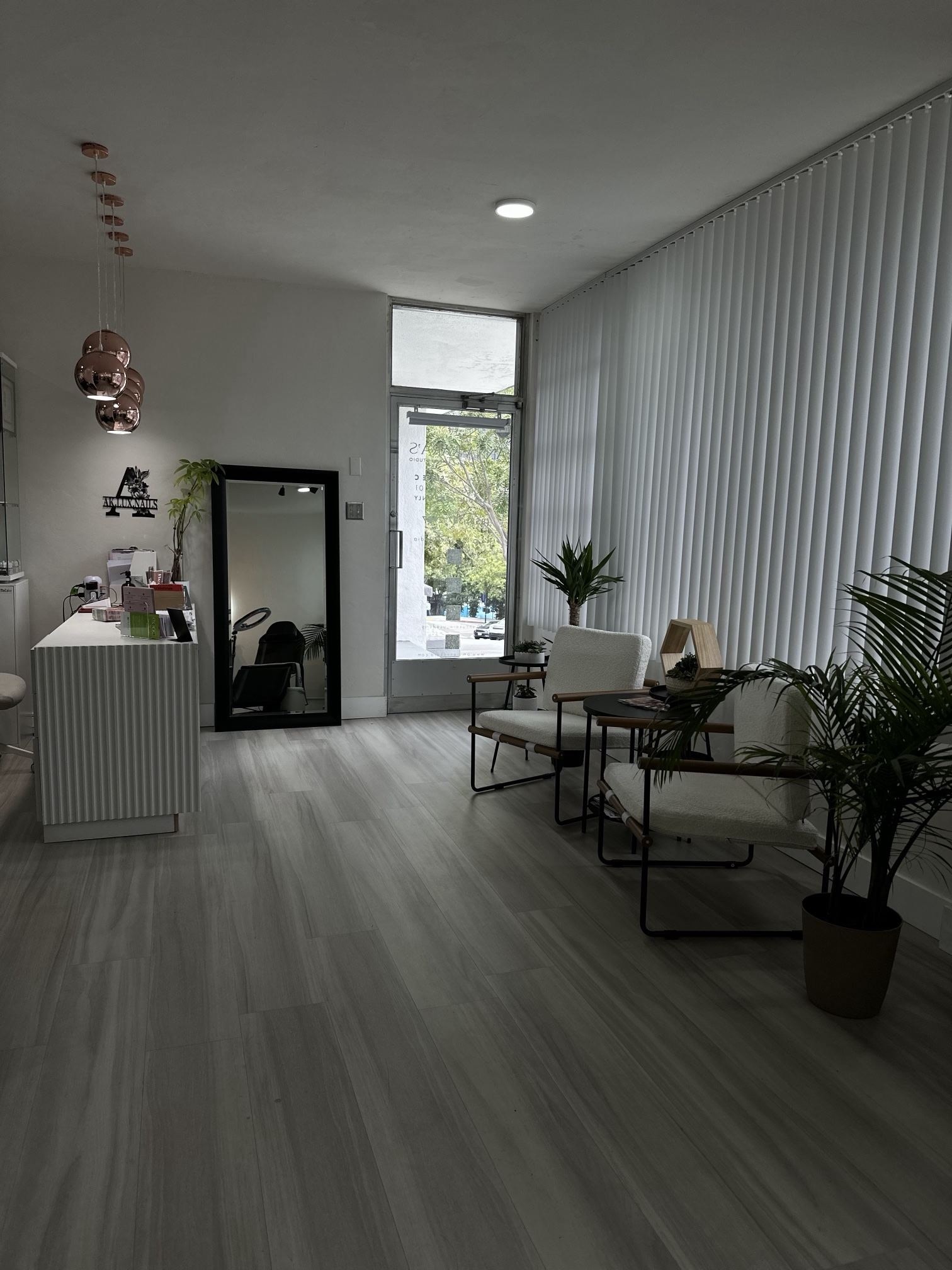 Reception lobby with a white ribbed desk, an AK.LUX.NAILS sign on the wall, a mirror and two white armchairs by the window